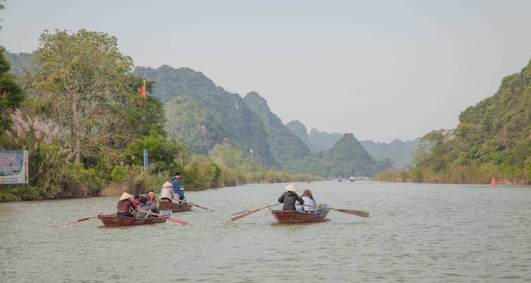 Verschillende boten met mensen die roeien op een brede rivier omringd door bergen.