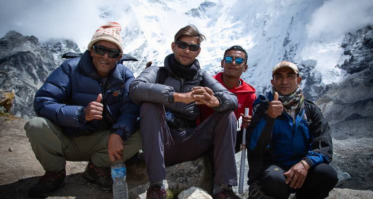 Cuatro trekkers con chaquetas de plumas posan sonriendo con un dramático telón de fondo de montañas cubiertas de glaciares.
