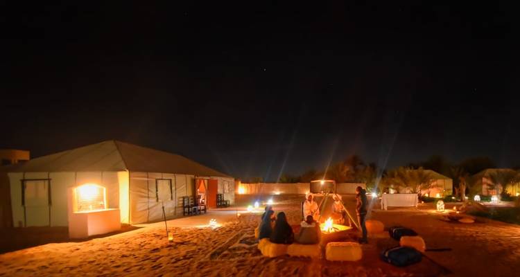 Nachtszene von Menschen, die um ein Lagerfeuer in Zelten sitzen.