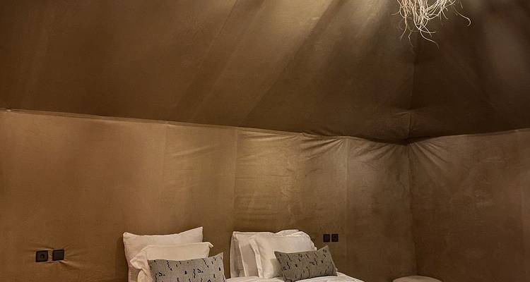 Interior acogedor del campamento desértico con tiendas de campaña que presenta tonos neutros, camas individuales y iluminación suave.