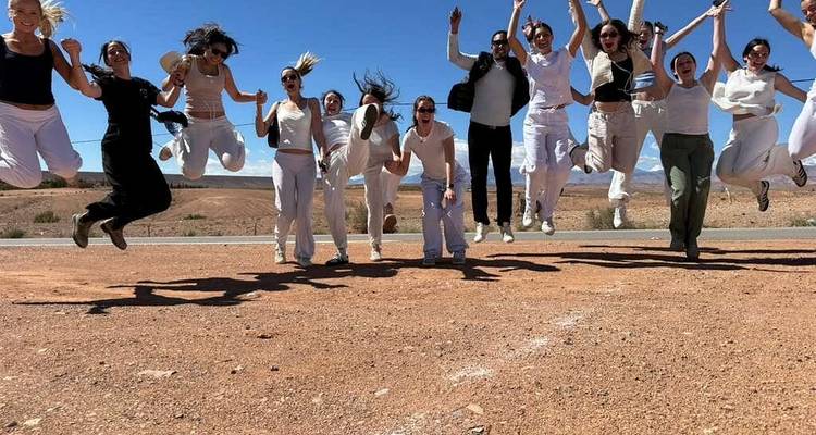 Grupo energético salta simultáneamente al costado de una carretera desértica bajo un cielo azul brillante.