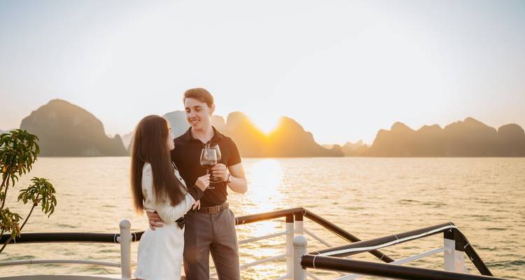 A couple enjoying a sunset on a boat with limestone formations in the background.