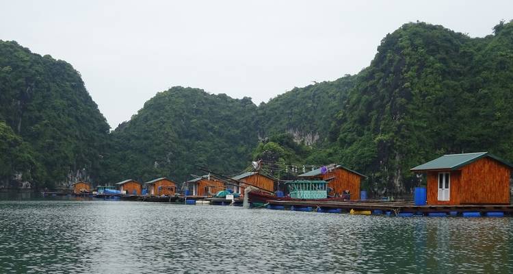 Maisons en bois flottant sur l'eau au milieu de collines calcaires.