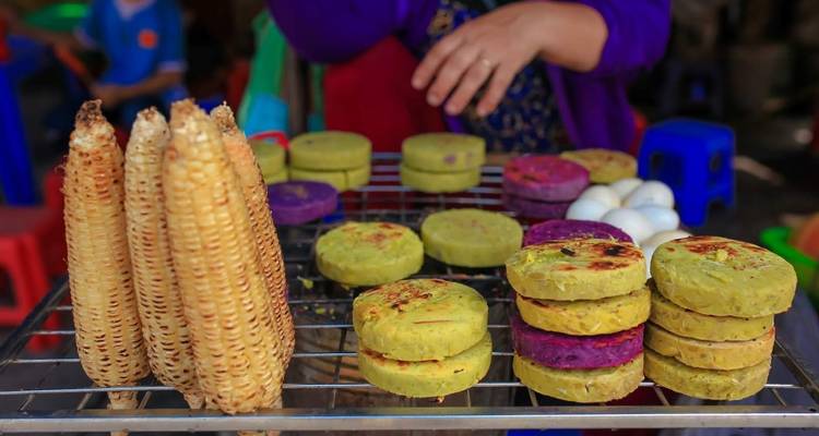 Maïs grillé et gâteaux de riz colorés à un stand de nourriture de rue.
