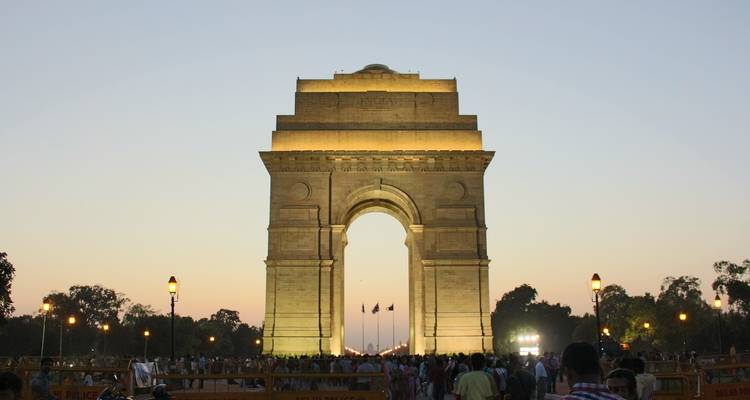 The India Gate at dusk with a crowd of people in front.