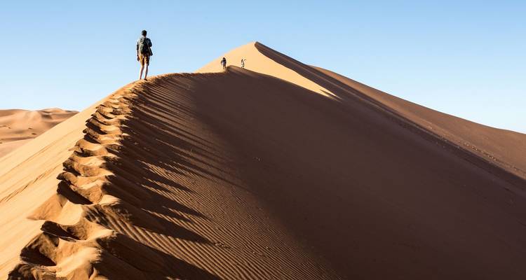 Un voyageur marchant le long de la crête acérée d'une dune de sable rouge imposante à Sossusvlei au lever du soleil.