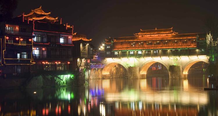 An illuminated traditional bridge and buildings reflected in water.