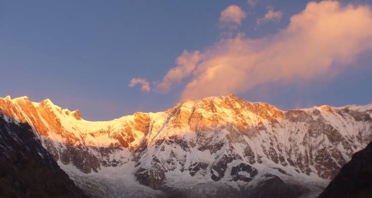 Chaîne de montagnes enneigées baignée de soleil avec des nuages dramatiques.