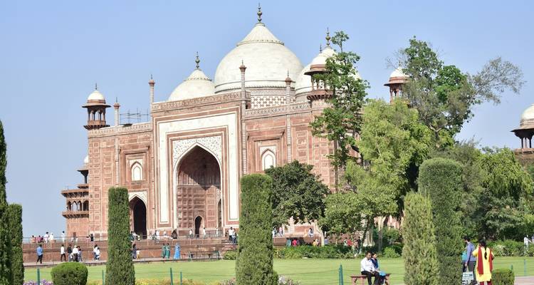 The ornate entrance of a historical building, surrounded by gardens and people.
