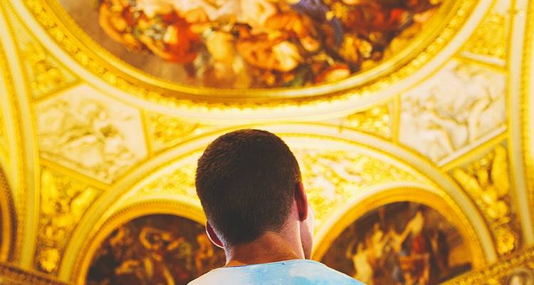 Jonge reiziger die omhoog kijkt naar een ingewikkeld gouden plafond versierd met klassieke frescos in een groot museum of kathedraal