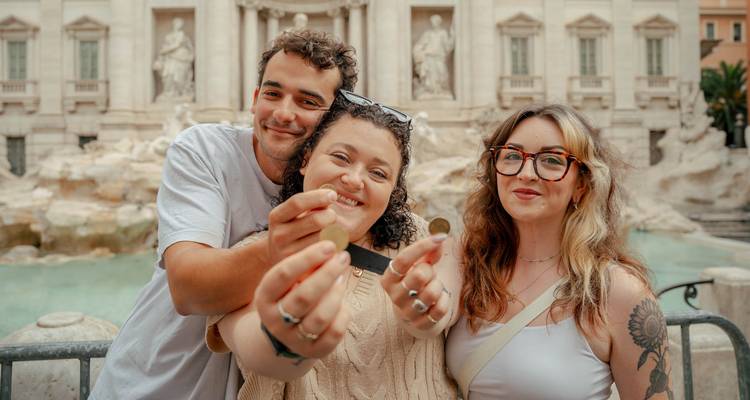 Drie reizigers houden trots munten vast terwijl ze voor Romes Trevi-fontein staan.