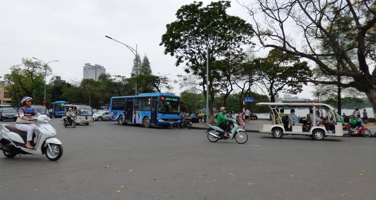 Busy urban street with a blue bus, scooters, and a rickshaw.