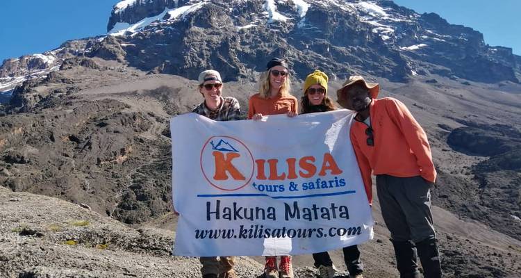 Trekkers posando con un banner de Kilisa Tours en las laderas del Monte Kilimanjaro bajo un cielo despejado.