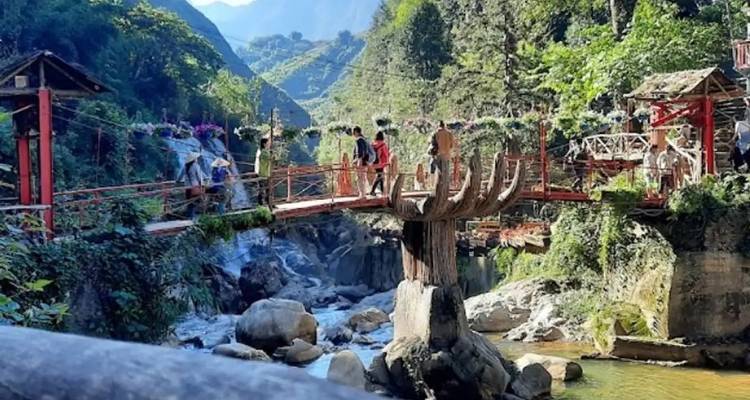 Brücke mit Menschen über steinige Stromschnellen in einem Dorf.