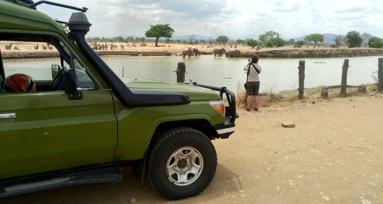 Ein Safari-Fahrzeug mit einer Person, die einen See fotografiert.