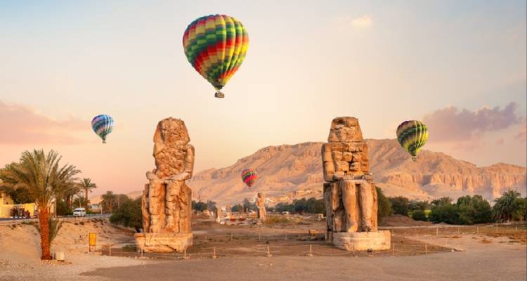 Globos aerostáticos sobre estatuas antiguas en un paisaje desértico.