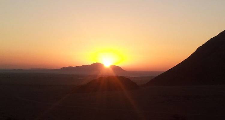 Golden sunrise over distant desert mountains with an orange sky