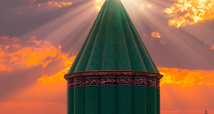 Mausolée conique aux tuiles vertes de Mevlana à Konya illuminé par les rayons du coucher de soleil.