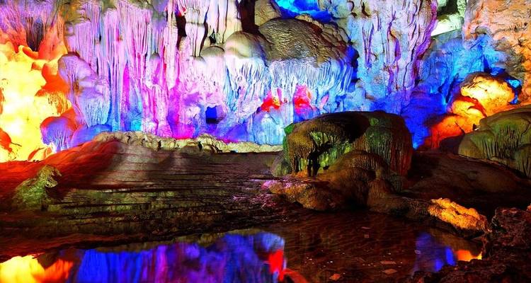Interior de cueva iluminado coloridamente con estalactitas y estalagmitas.