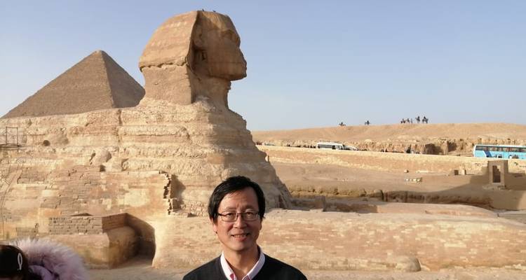 Een persoon die staat bij de Sfinx en een piramide in Giza, Egypte.