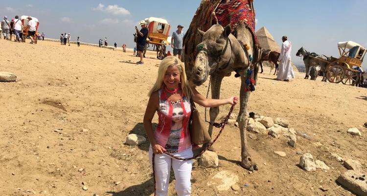 Woman standing next to a camel in a desert-like area.