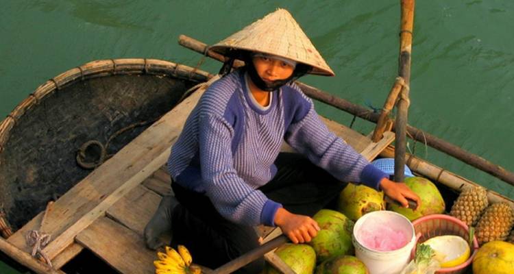Personne dans un petit bateau avec des fruits sur une rivière.