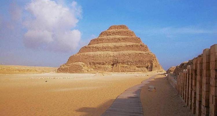 Pyramide à degrés de Djéser s'élevant du désert sablonneux de Saqqara sous un ciel bleu parsemé de nuages épars