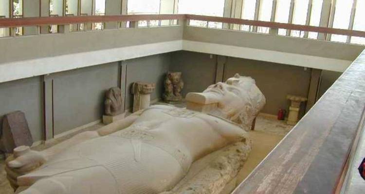 Une colossale statue de Ramsès II allongée repose à l'intérieur d'une fosse de musée entourée de murs d'exposition et d'artefacts.