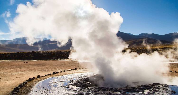 Vapor elevándose desde un campo de géiseres con un telón de fondo montañoso.