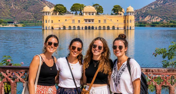Vier lachende vrienden poseren met het drijvende paleis Jal Mahal en de Aravalli-heuvels achter hen.