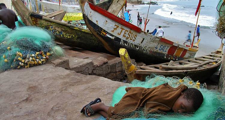 Un enfant dormant sur des filets de pêche près de bateaux peints sur une plage.