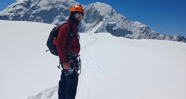 Bergsteiger steht auf einem schneebedeckten Pfad mit einer Berglandschaft im Hintergrund.