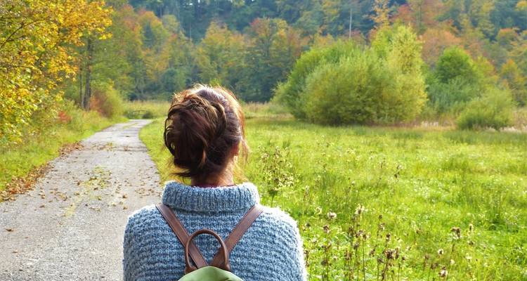 Une personne debout sur un sentier entourée de verdure et de feuillage d'automne.