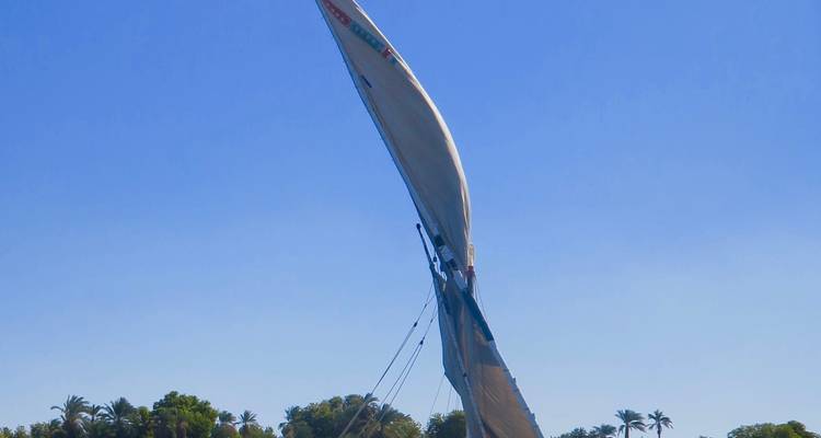 Een felukka zeilboot op de Nijl, met het zeil gehesen tegen een heldere blauwe lucht.