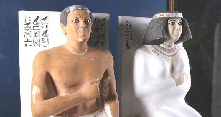 Twee oude standbeelden, één mannelijk en één vrouwelijk, met hiërogliefen op de achtergrond.