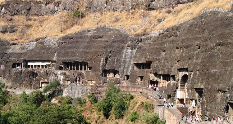 Anciennes grottes taillées dans la roche avec des visiteurs explorant la zone.