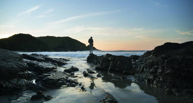 Silueta de una persona en las rocas de una playa durante el atardecer.