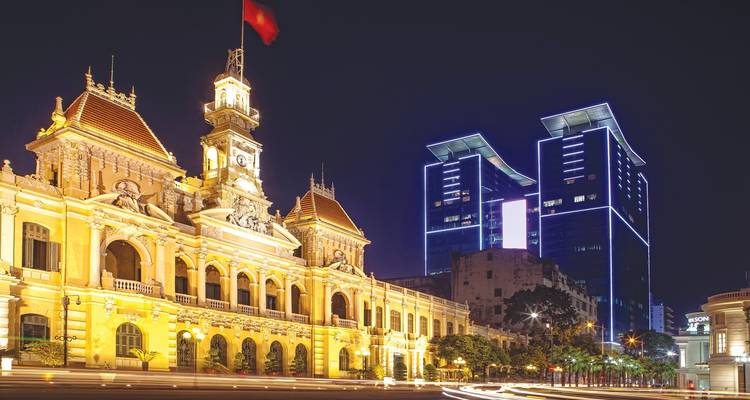 Edificio iluminado de la época colonial junto a rascacielos modernos por la noche.