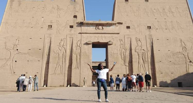 Los visitantes exploran y fotografían la fachada monumental de un templo egipcio antiguo adornado con jeroglíficos.