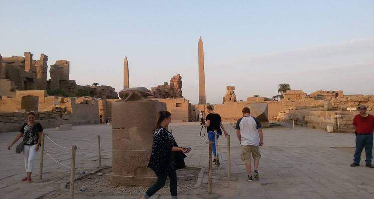 Los turistas deambulan entre obeliscos antiguos y ruinas dentro de un vasto complejo de templos egipcios al atardecer.