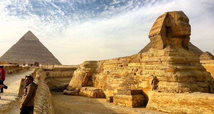 La Gran Esfinge y una pirámide se alzan majestuosamente bajo un cielo texturizado mientras los visitantes admiran el sitio.