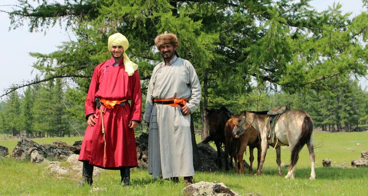 Zwei Personen in traditioneller Kleidung mit Pferden in einem Waldgebiet.