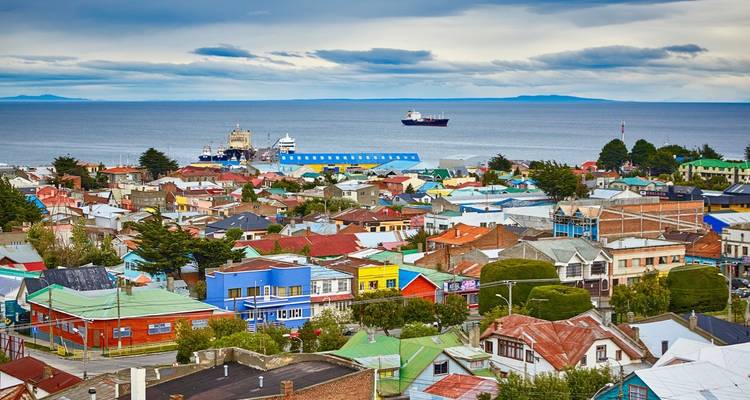 Panoramic view over colorful rooftops of a coastal town with ships anchored offshore.