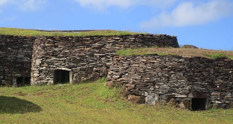 Ancient stone dwellings built into a grassy hillside beneath a bright blue sky.