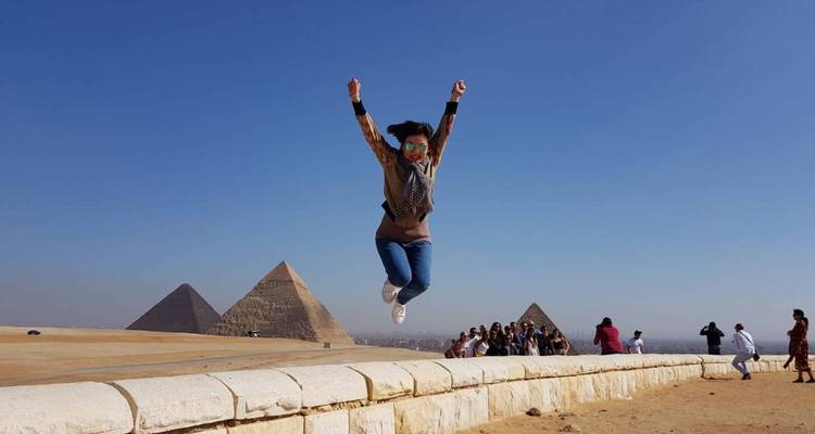 Reisender springt freudig vor den Pyramiden in die Luft, während die Reisegruppe in der Ferne zu sehen ist
