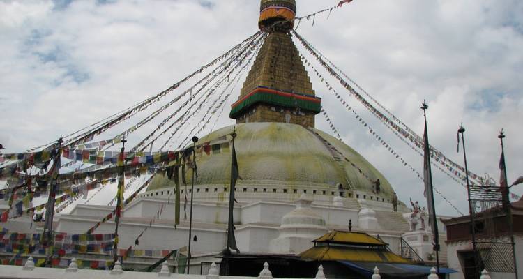 Enorme domo blanco de la Estupa de Boudhanath cubierto de coloridas banderas de oración contra un cielo nublado.