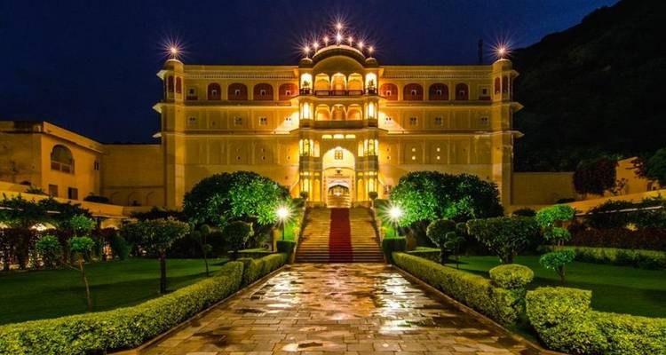 Illuminated mansion with a garden and red carpet at night.