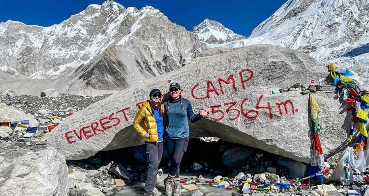 Zwei Personen posieren neben einem 'Everest Base Camp'-Schild auf einem Felsen.
