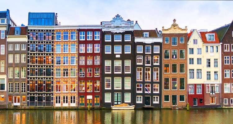 Primera fila de casas coloridas y estrechas del canal en Ámsterdam reflejadas en agua inmóvil.