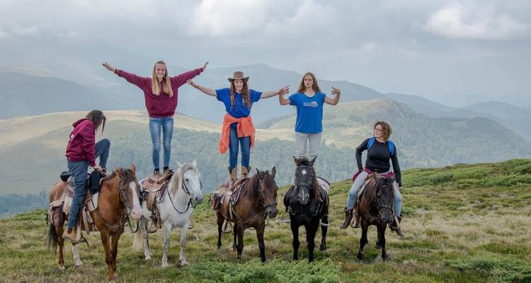 Cinco personas de pie sobre caballos en un paisaje montañoso.